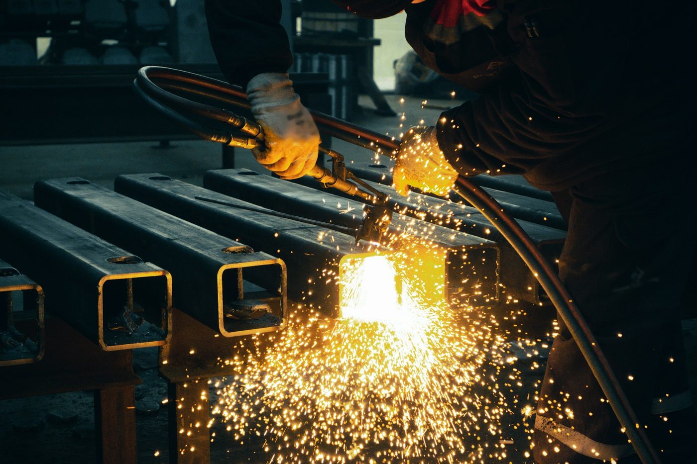 Fabricator cutting steel box sections with sparks in a workshop