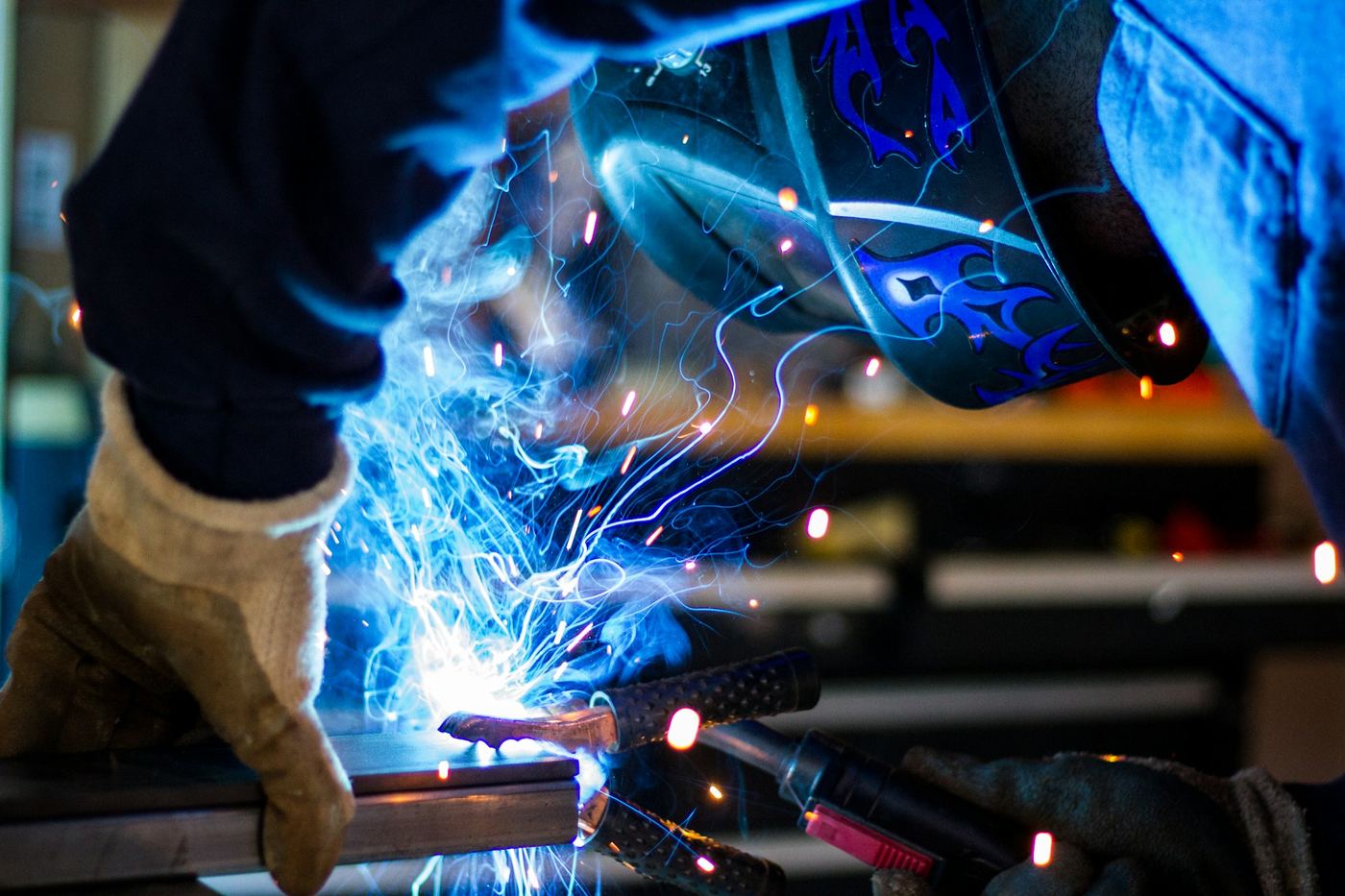 Close-up of a welder in gloves and helmet welding with bright sparks