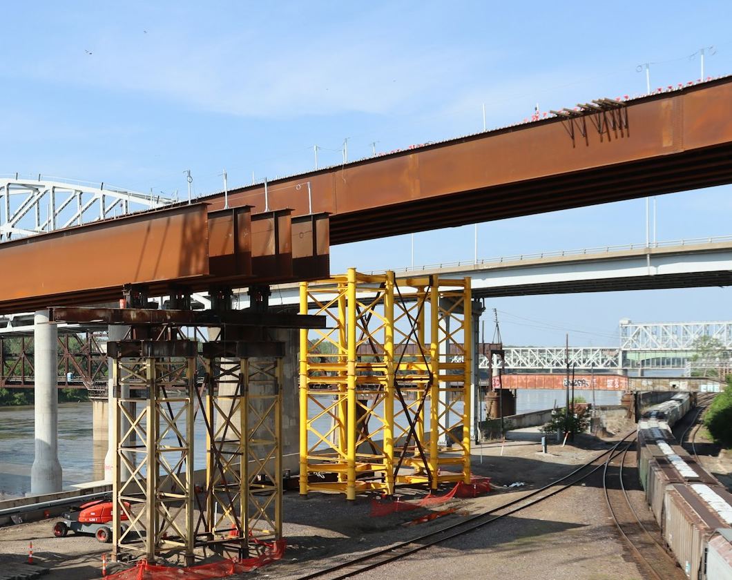 Steel bridge girders supported on temporary towers beside a rail line