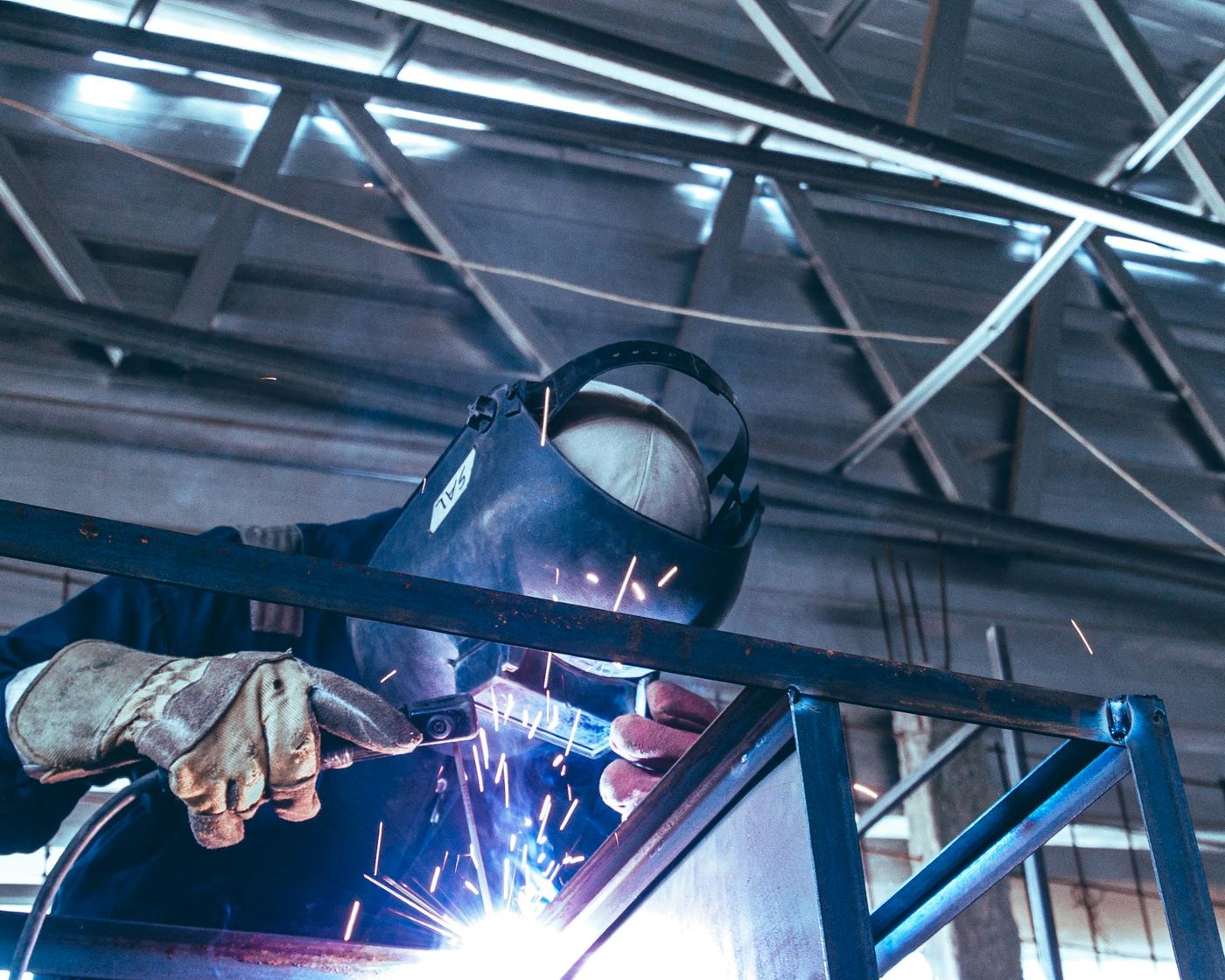 Welder in a helmet and gloves welding a steel frame in a fabrication workshop